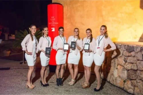 Sechs Hostessen mit Lanyards und Geräten in der Hand vor einer roten ProSieben-Säule mit dem Slogan We love to entertain you