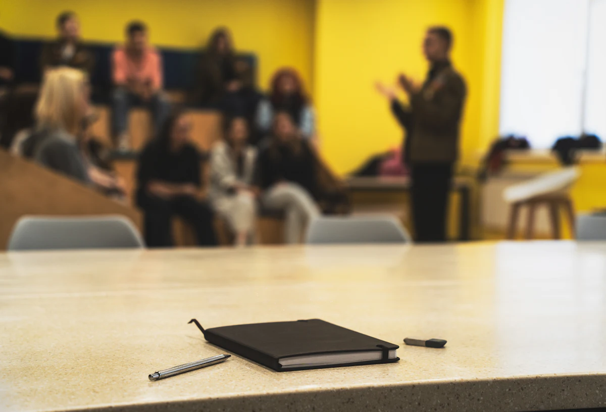 Notebook and pens on a table, with the audience and a speaker blurred in the background